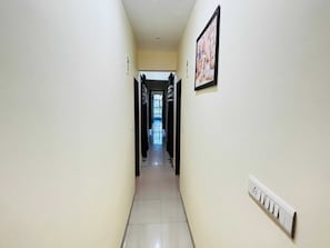 A narrow hallway with a tiled floor, a light switch on the wall, and a framed picture. - Classic Hotel Nitin Inn (Ujjain)
