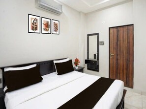 A hotel room with a bed, a nightstand, a mirror, and a door. - Classic Hotel Nitin Inn (Ujjain)
