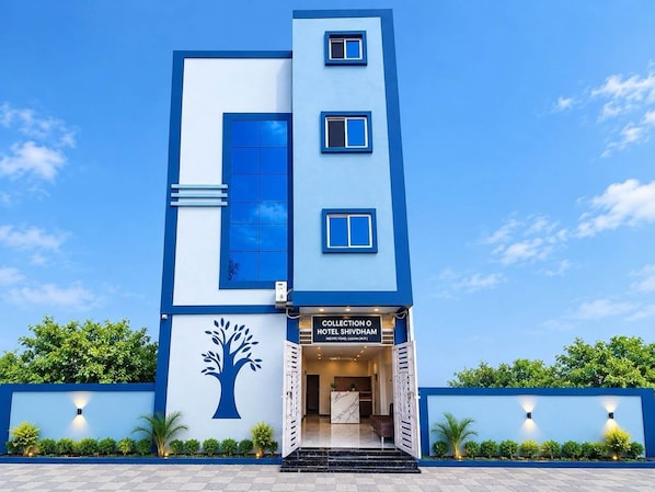 A modern hotel with a blue and white facade, a tree mural, and a sign for 'Collection O Hotel Shivdham.' - Classic Hotel Nitin Inn (Ujjain)