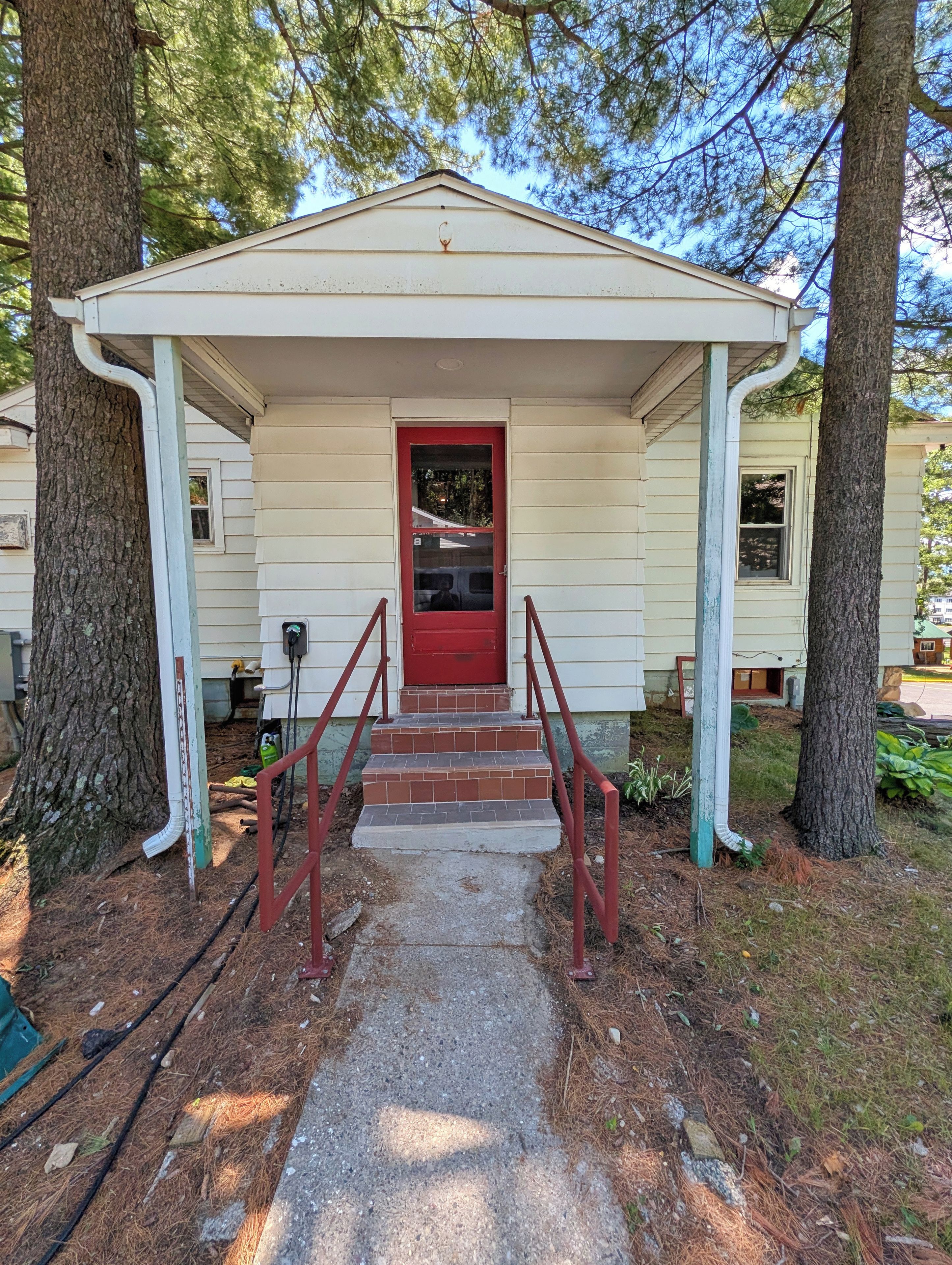 A covered porch with a red door, steps, and a railing.
