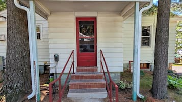 A covered porch with a red door, steps, and a railing.