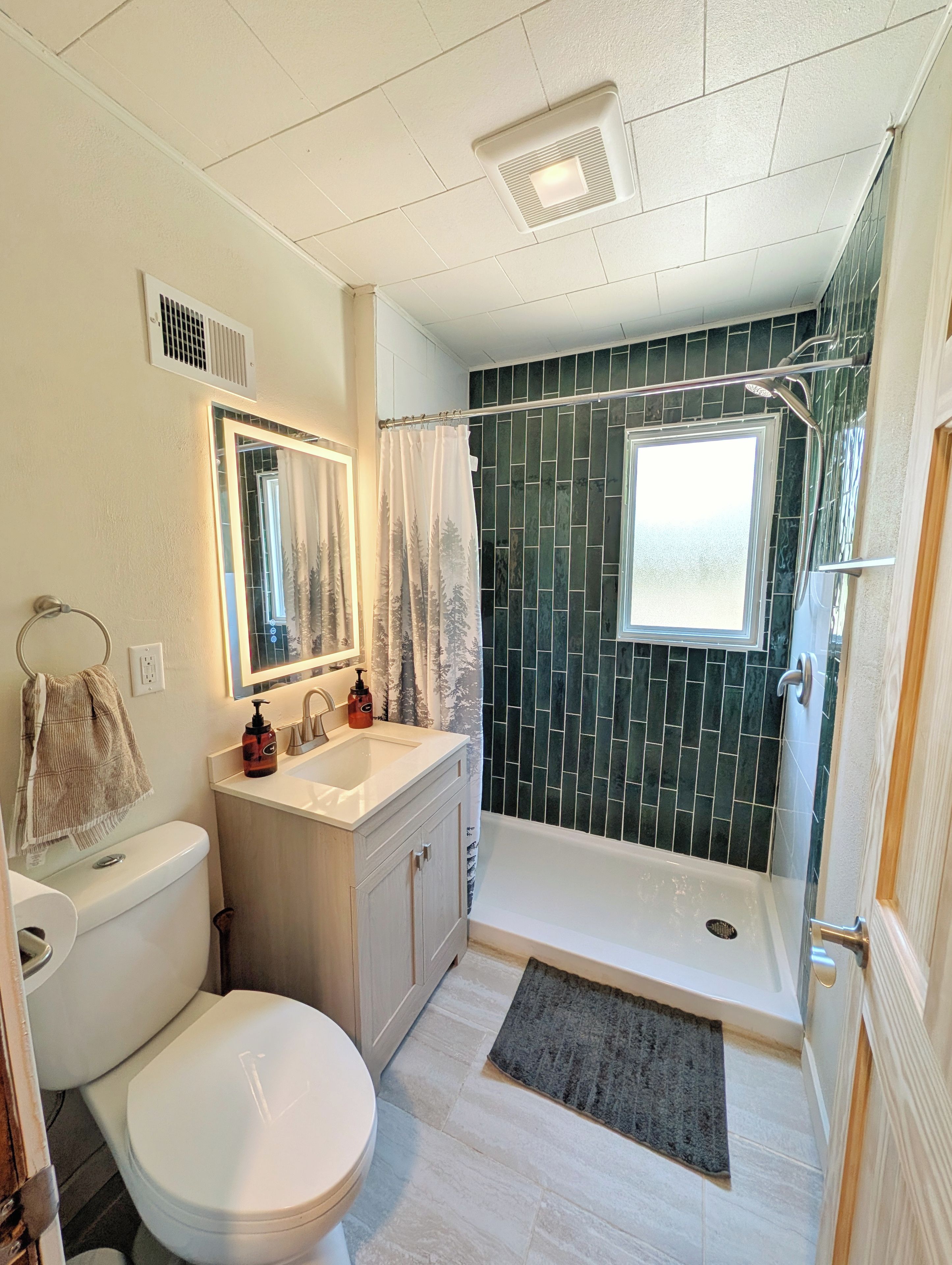 A bathroom with a toilet, sink, shower, and a window.