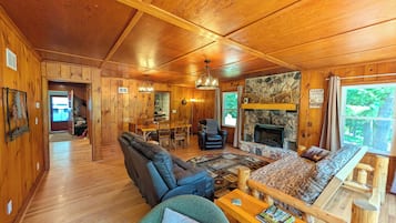 A cabin interior with a fireplace, wooden walls, a dining area, and a sofa.