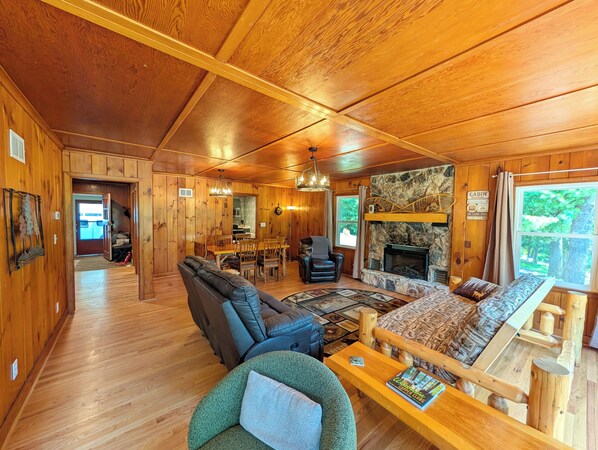 A cabin interior with a fireplace, wooden walls, a dining area, and a sofa.