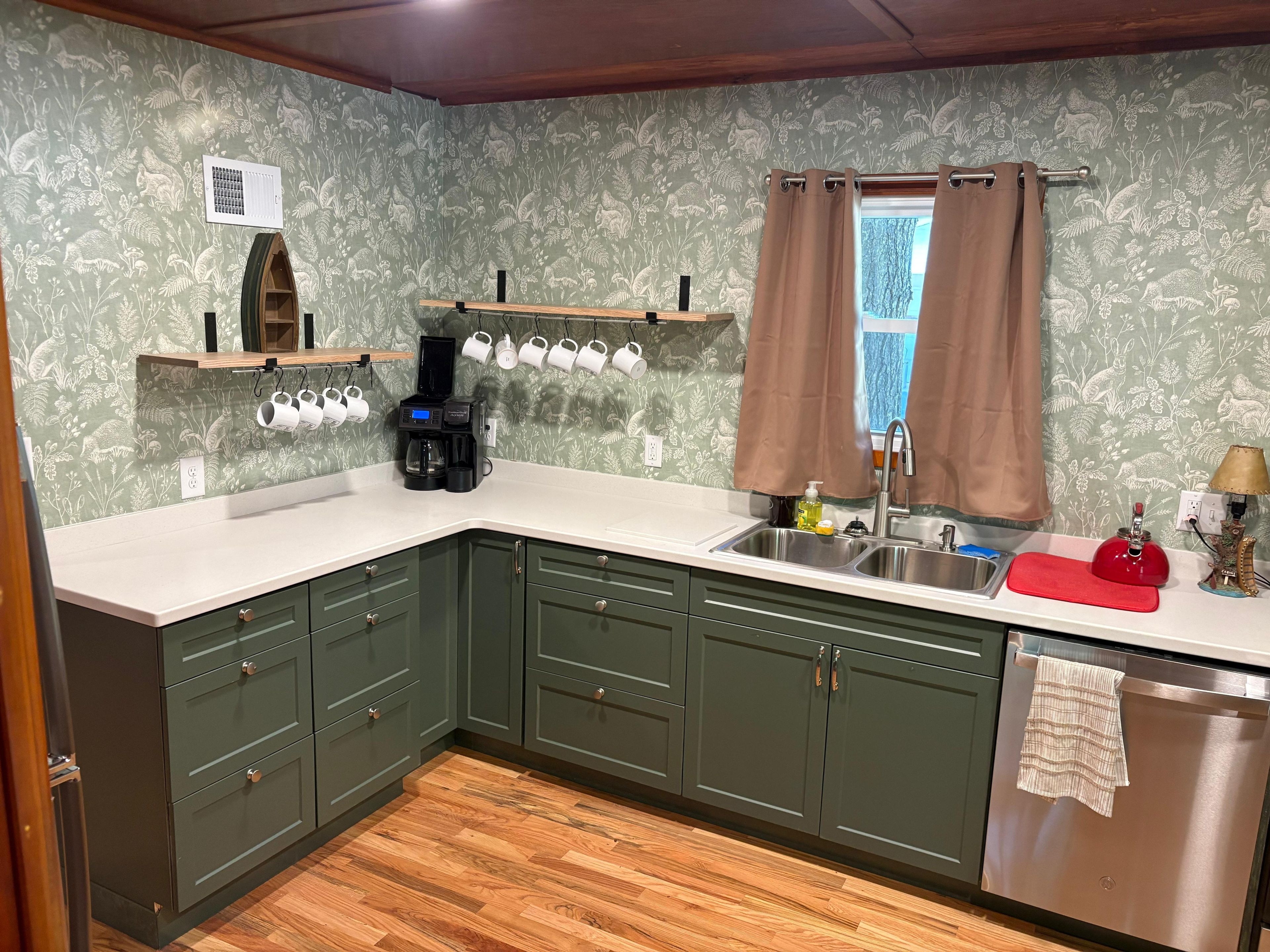 A kitchen with green cabinets, a coffee maker, a sink, and a window with curtains.