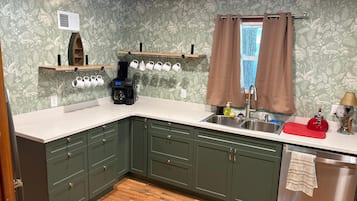 A kitchen with green cabinets, a coffee maker, a sink, and a window with curtains.