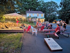 An outdoor gathering with a stage, seating, and a wooden sign indicating a bar.