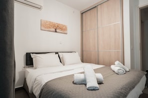 Una cama bien hecha con ropa blanca y una colcha acolchada, un cuadro en la pared y un armario de madera.