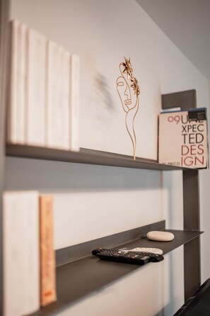 Una parete con un'opera d'arte in metallo decorativo, un libro intitolato 'OUP XPEC TED DESIGN' e un telecomando su uno scaffale.