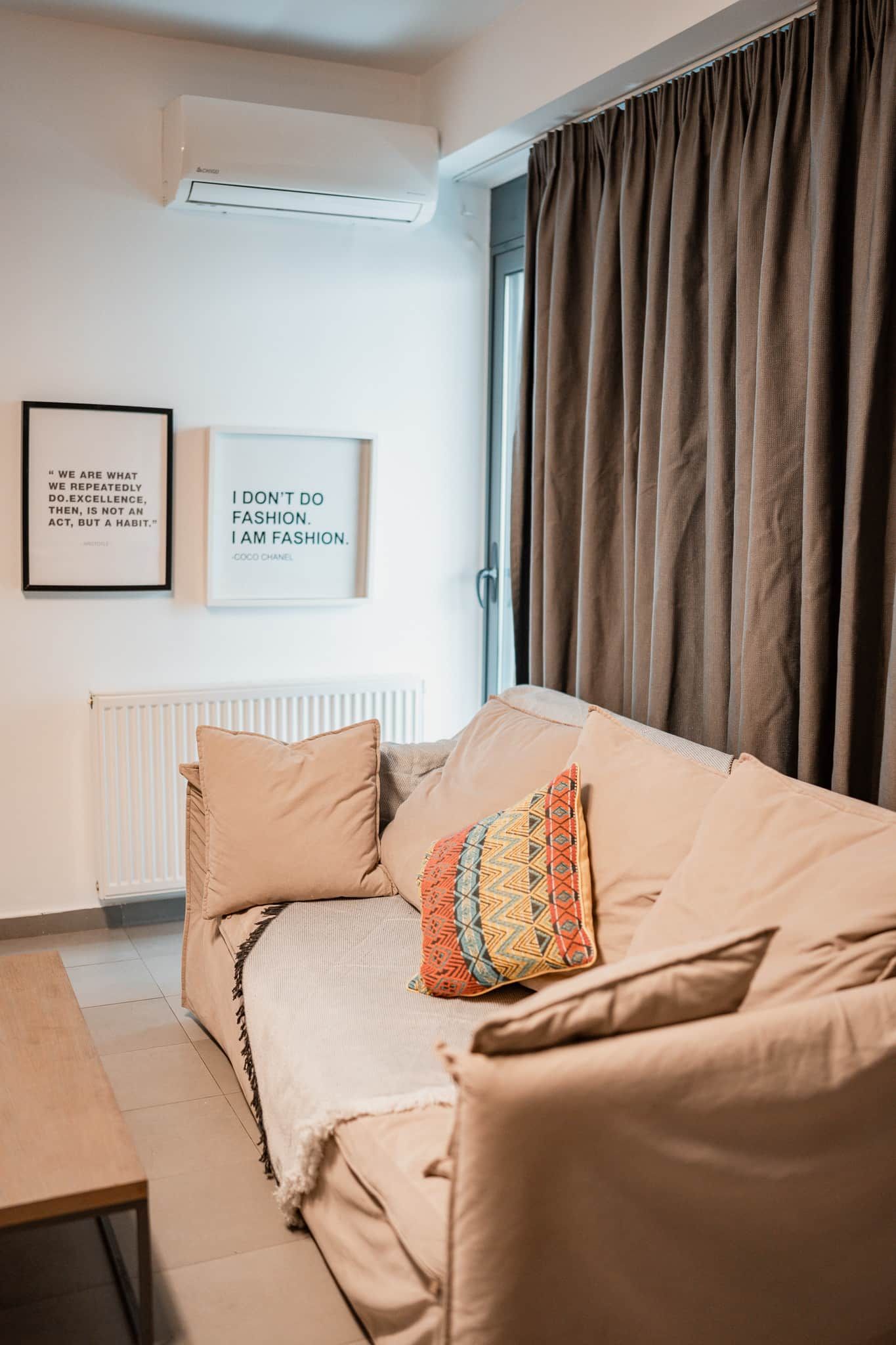 Un soggiorno moderno con un divano color beige, un cuscino decorativo e due quadri con citazioni appese al muro.