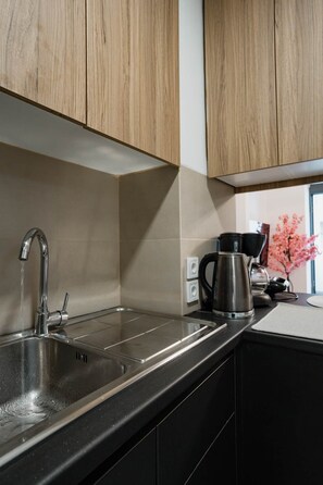 Una cucina con lavello in acciaio inox, mobili in legno, una macchina da caffè e una finestra vista fiori rosa.