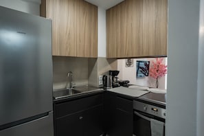 Una cucina compatta con frigorifero in acciaio inossidabile, lavello, macchina del caffè e display digitale del forno.