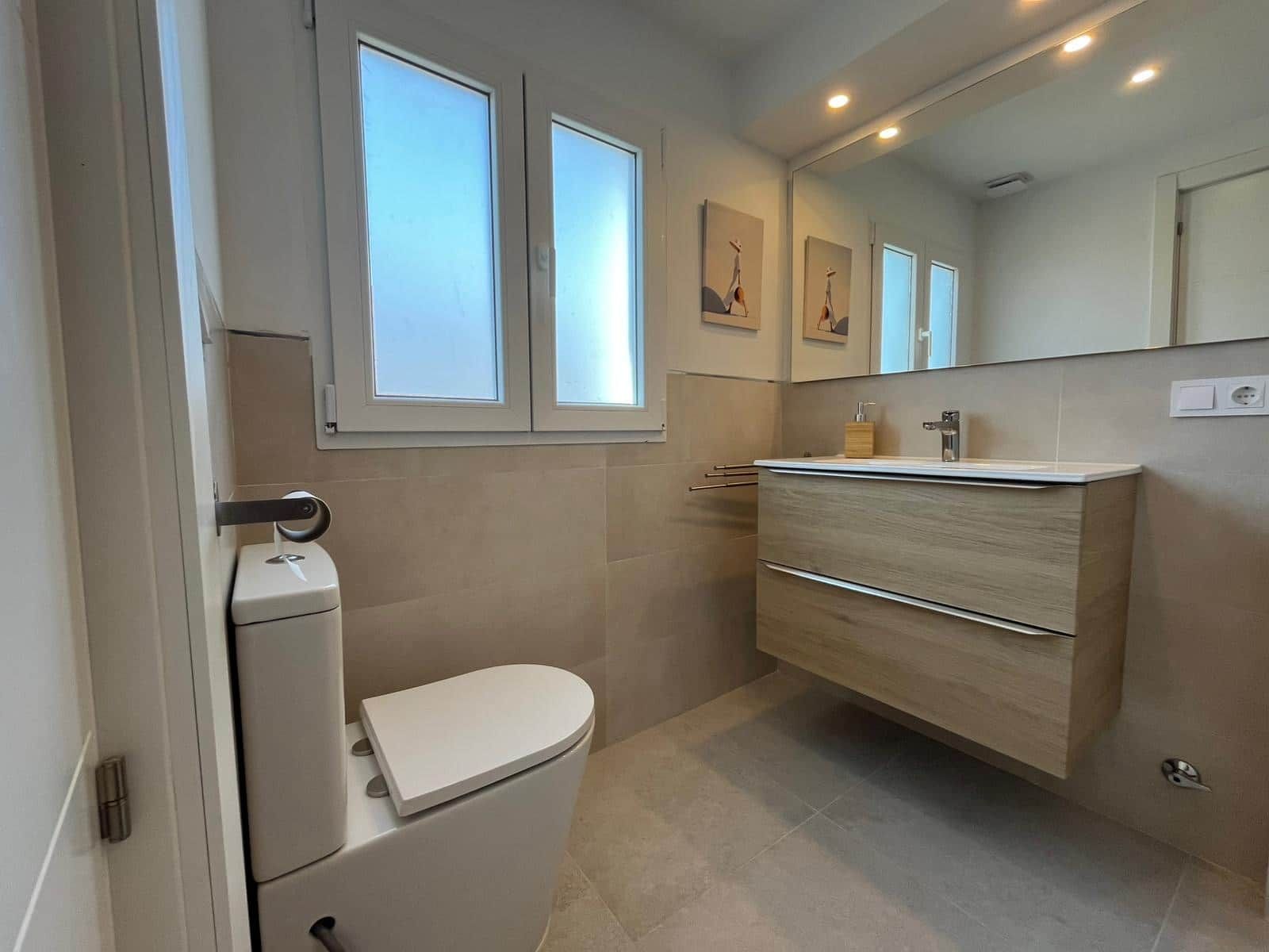 A modern bathroom with a toilet, vanity, and a large mirror.