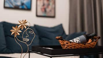Un soggiorno moderno con un tavolino da caffè nero, un'opera d'arte in fili metallici, un cesto intrecciato con una bottiglia e un divano con un cuscino blu.
