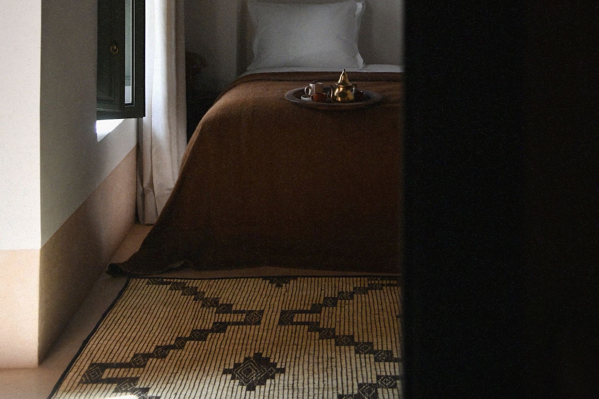 A bedroom with a bed, a window, and a patterned rug.