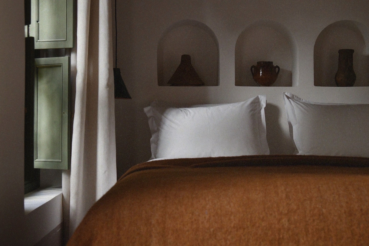A bedroom with a bed, pillows, and a wall-mounted shelf with decorative items.