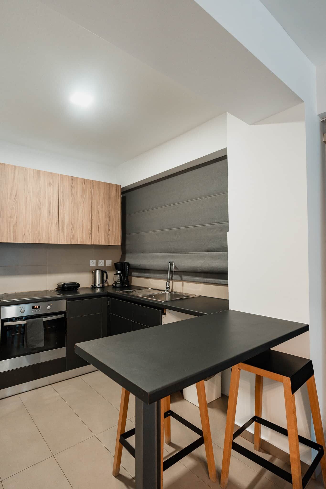 Una cucina moderna con un piano di lavoro nero, mobili in legno, forno integrato e schienale grigio.