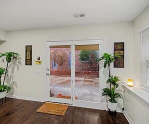 A room with a sliding glass door leading to a brick patio, a doormat, and two potted plants.