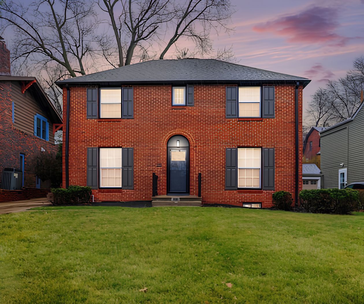A two-story brick house with a front entrance, a small front porch, and a well-maintained lawn.