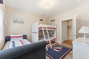 A bedroom with bunk beds, a desk, a chair, a lamp, and a rug with a nautical design. - Wildwood Crest 3BR/2BA condo with pool-view deck (Wildwood Crest)