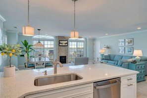 A modern kitchen with a central island, a dining area with a white table and chairs, and a living room with a blue sofa and decorative lamps. - Bay-view 3BR/2BA Condo with balcony (Wildwood Crest)