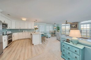 A modern kitchen with white cabinetry, a central island, and a dining area with a view. - Bay-view 3BR/2BA Condo with balcony (Wildwood Crest)