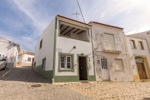 Un edificio de dos pisos con fachada verde y blanca, una entrada visible y un balcón en el piso superior.