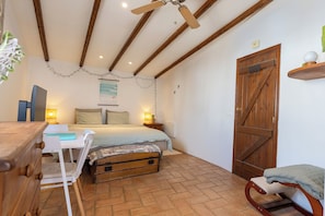 Een slaapkamer met een bed, nachtkastjes, een bureau, een stoel, een houten garderobe, een houten deur en een plafondventilator.