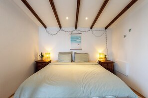Un dormitorio con cama, dos mesitas de noche, un cuadro en la pared y un techo con vigas de madera.