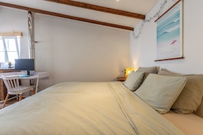 A bedroom with a bed, a desk with a computer, and a wall-mounted lamp.
