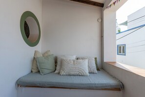 Un pequeño espacio de descanso con banco y cojines, un espejo en la pared y ventana con vistas a un edificio.