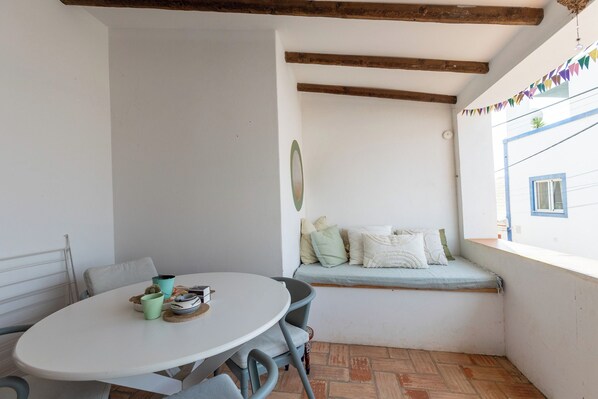 A small, enclosed patio area with a round table and chairs, a cushioned bench, and a view of the outside.