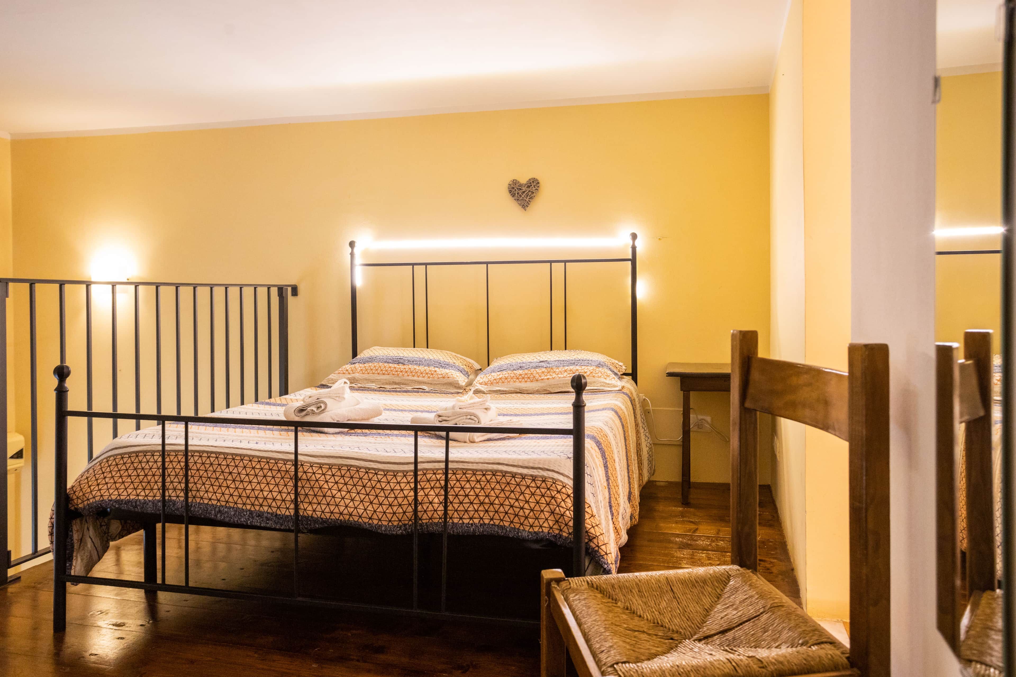 Un lit simple avec un cadre en métal, une table de chevet, une chaise et un décor mural en forme de cœur.