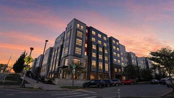 A multi-story residential building with a modern architectural design, featuring a mix of glass and concrete facades, and a pedestrian crossing in front.