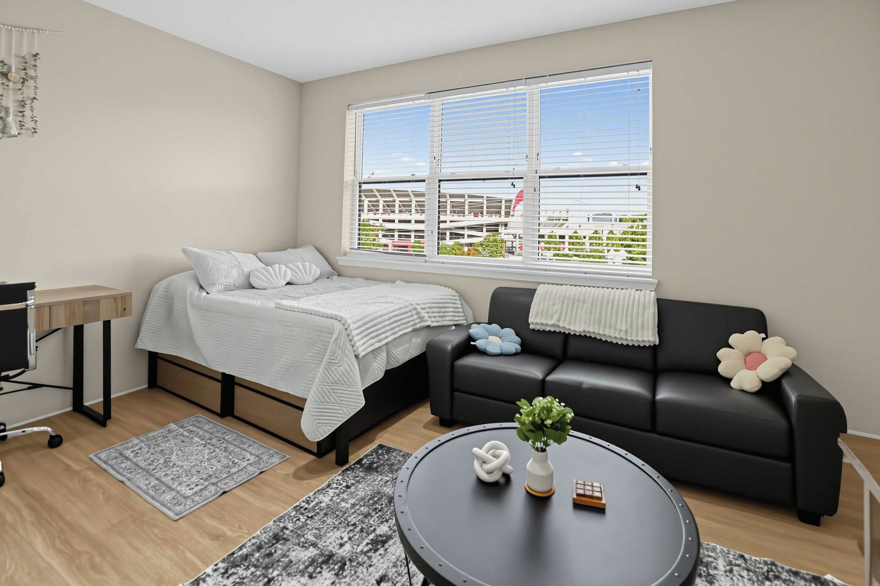 Una sala de estar moderna con una cama, un sofá negro, una mesa de centro con una planta y un ventanal con vistas a edificios.