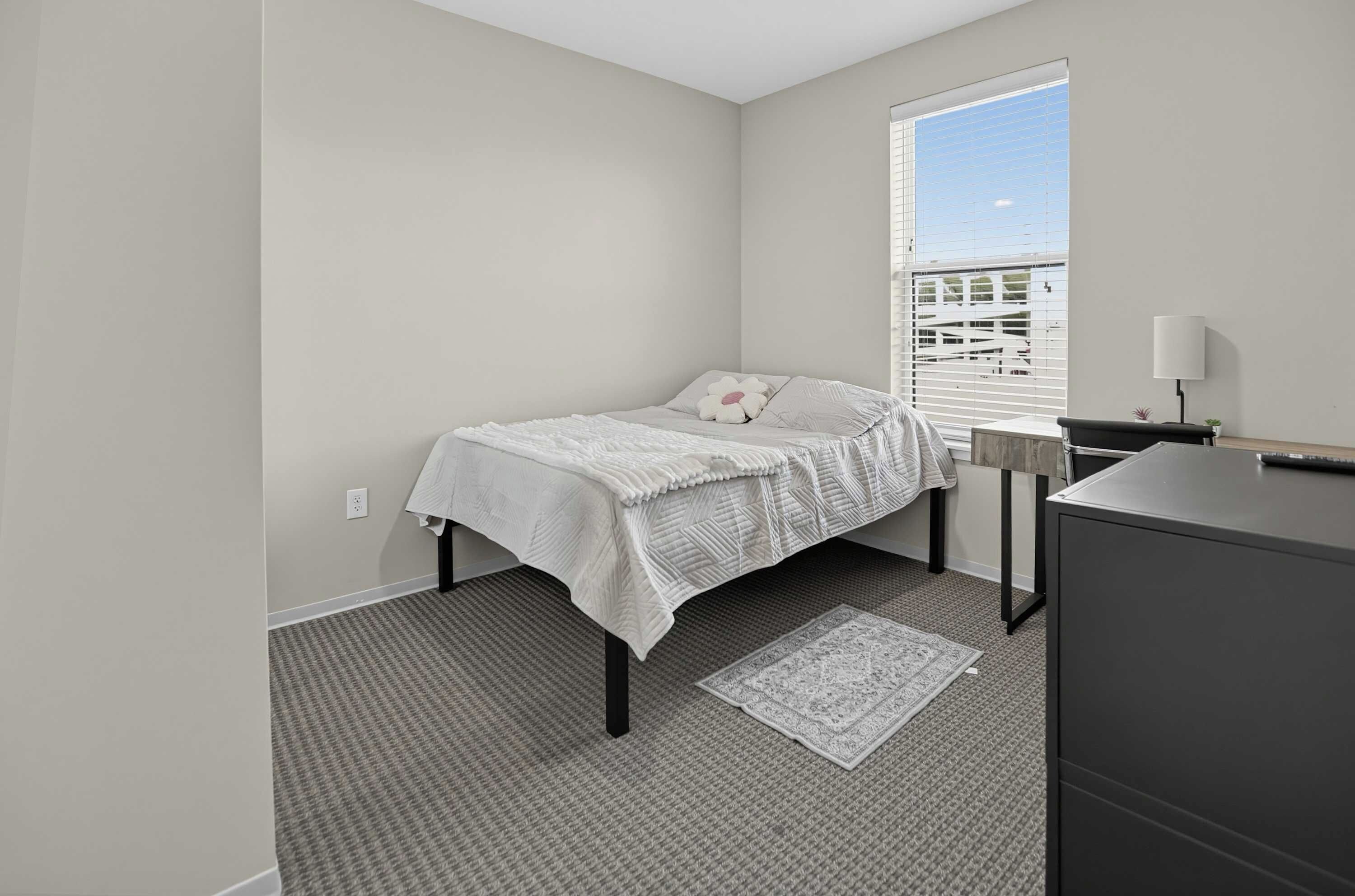 A bedroom with a bed, a nightstand, a lamp, and a window with blinds.