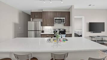 A modern kitchen with a large island, stainless steel appliances, and a flat-screen TV mounted on the wall.