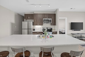 Una cocina moderna con una isla grande, electrodomésticos de acero inoxidable y un televisor de pantalla plana montado en la pared.