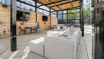 An outdoor seating area with a wooden ceiling, a flat-screen TV mounted on the wall, and a seating arrangement consisting of sofas and chairs.