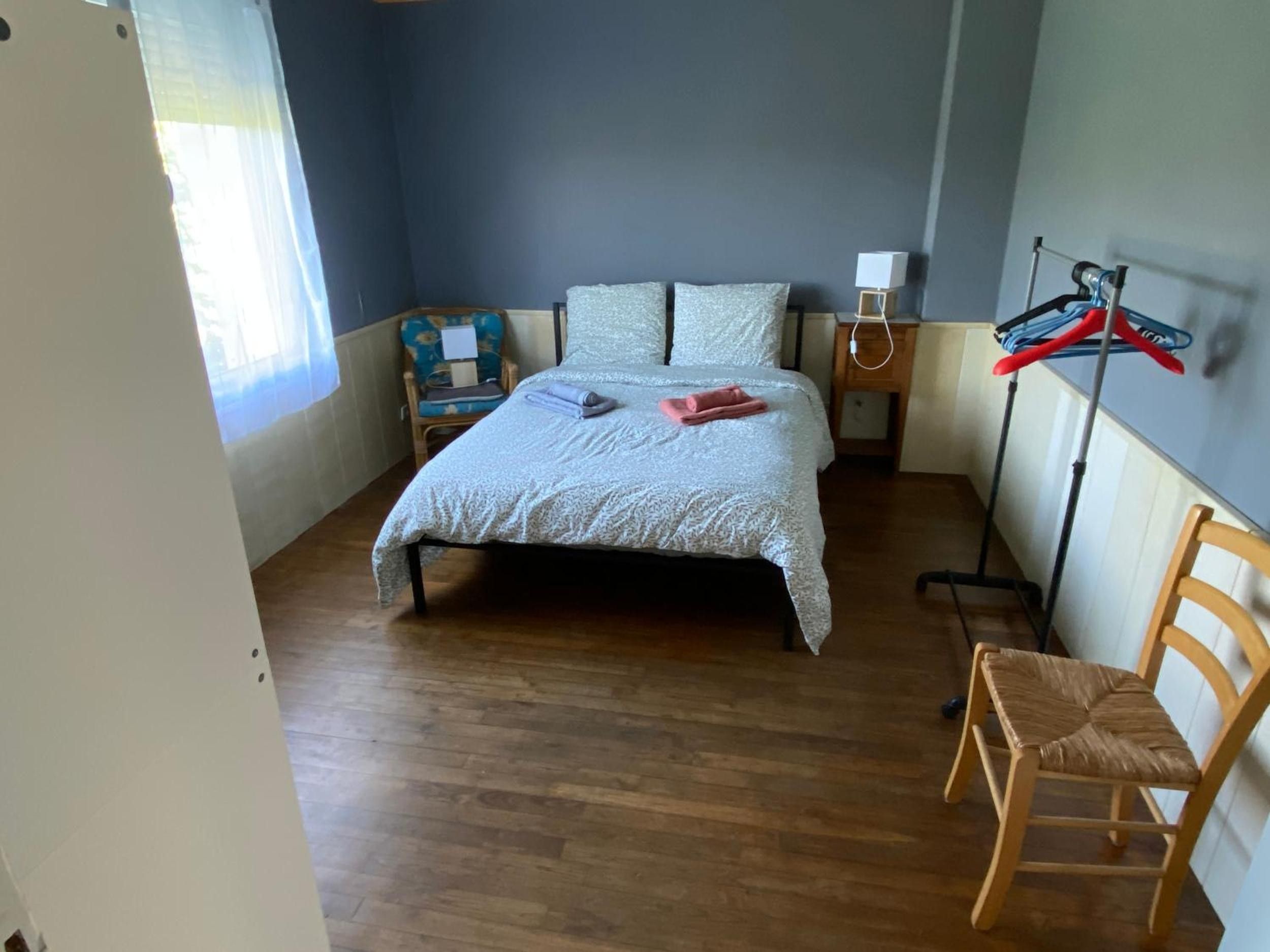 Un dormitorio con cama, una silla, una mesita de noche, una lámpara y un tendedero.