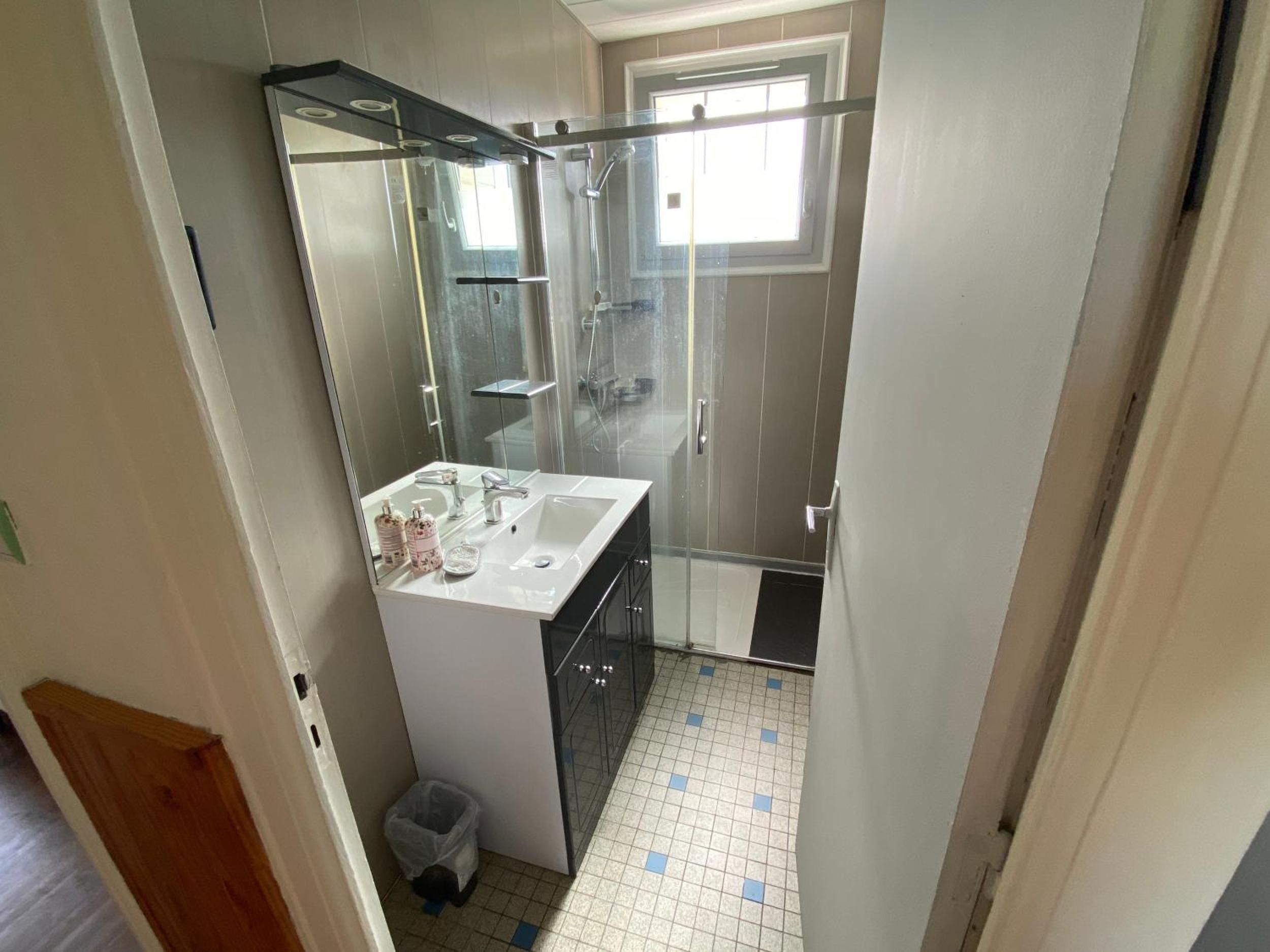 A compact bathroom with a glass shower enclosure, a white sink, and a small trash bin.