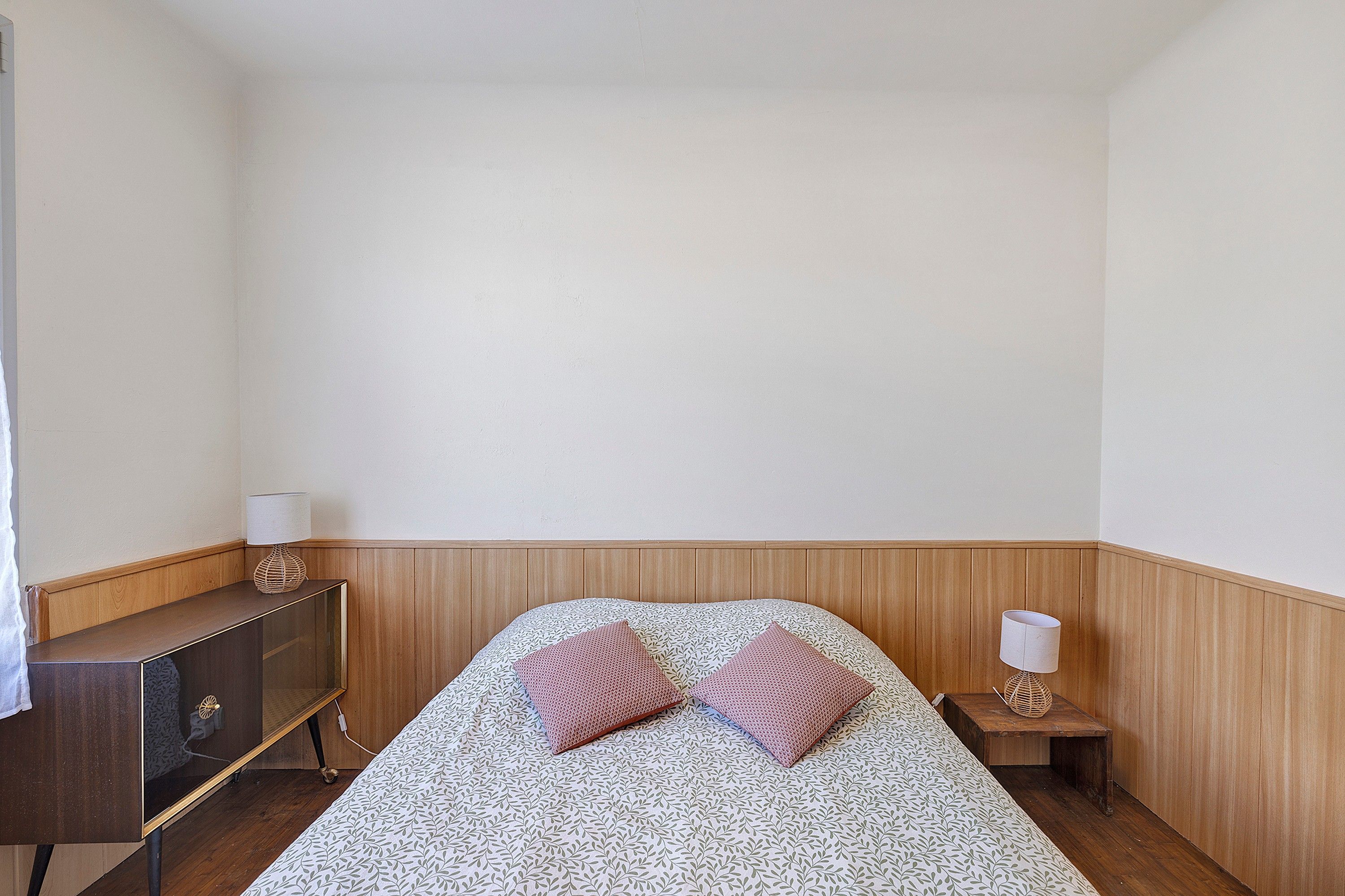 Ein schlichter, schlichter Schlafzimmer mit Bett, zwei Kissen, einem Nachttisch und einer Lampe.