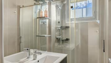 A modern bathroom with a glass-enclosed shower, a white sink, and a window providing natural light.