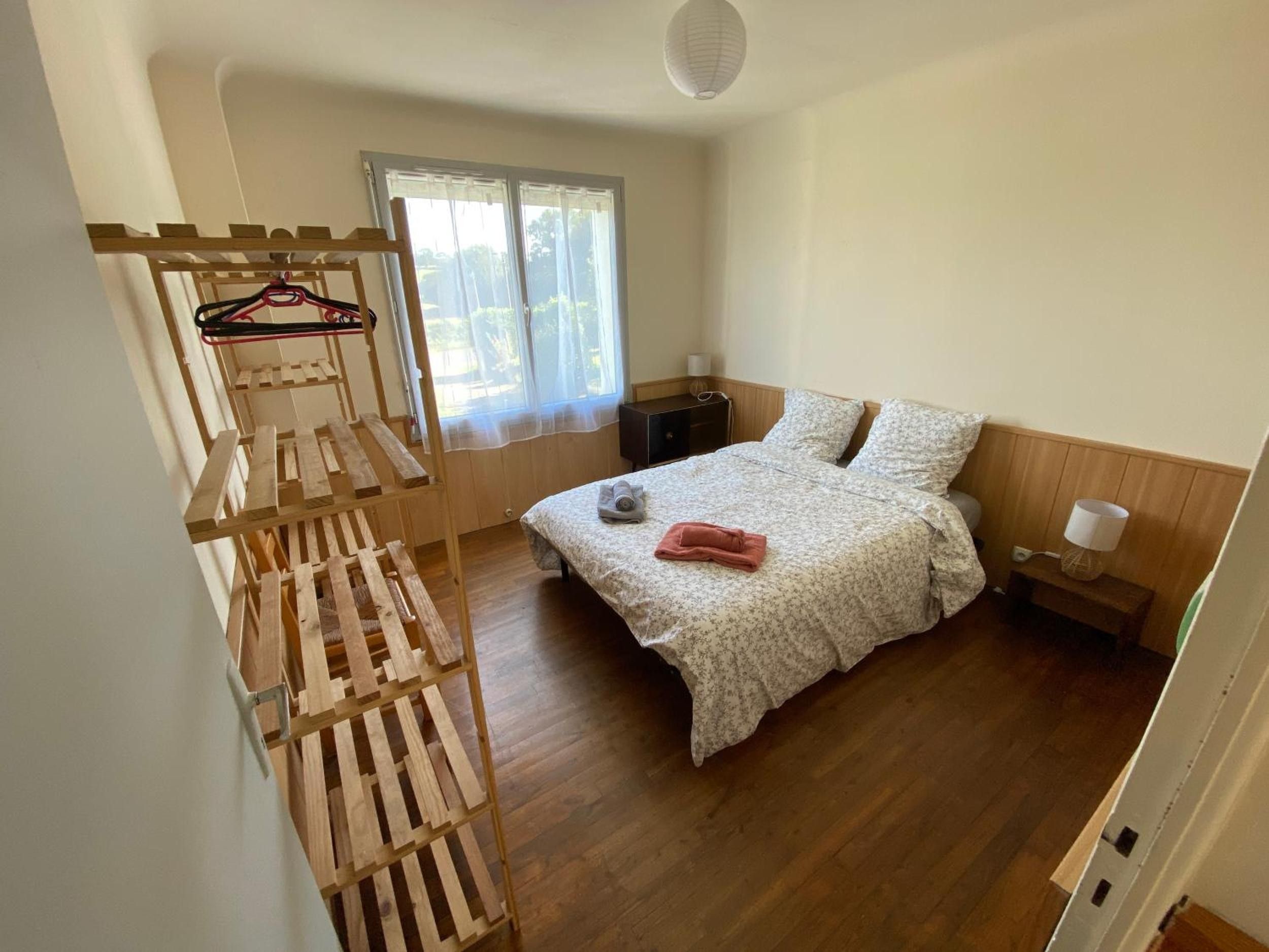 A bedroom with a bed, a wooden rack, a window, and a bedside table.