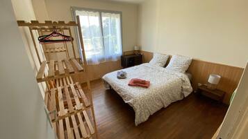 A bedroom with a bed, a wooden rack, a window, and a bedside table.