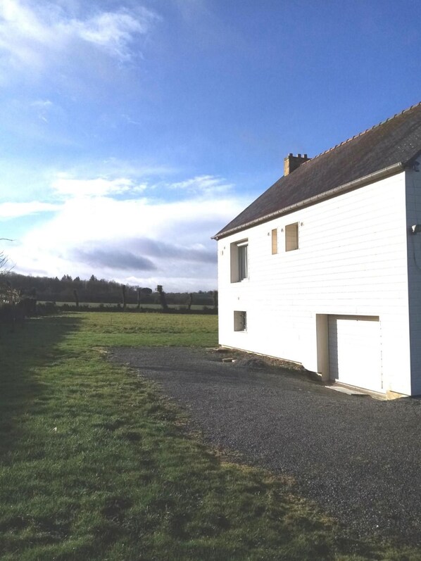 Un edificio blanco con un camino de grava y un campo verde al fondo.