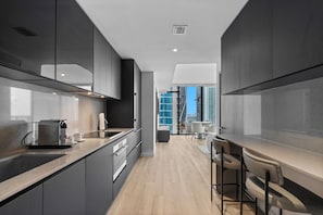 A modern kitchen with dark cabinetry, a wooden countertop, and a view of high-rise buildings through large windows. - 40th Floor Luxury E11EVEN Panoramic Bay & City View Suites (Miami)