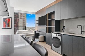 A modern kitchen with a built-in washer, a dining area with a large table and chairs, and a city view through the window. - E11EVEN Executive Level Suite | Pool & City Views (Miami)