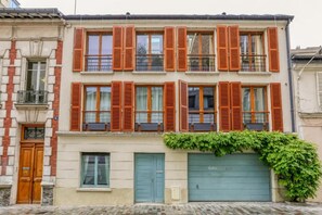 A multi-story building with a row of windows and shutters, a garage door, and a small balcony. - Luxury 150 m² Paris Duplex with Private Garden Terrace (Paris)