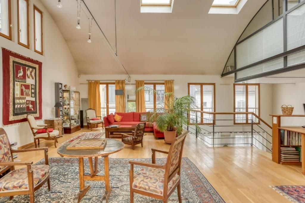Una sala de estar amplia con techo alto, un sofá rojo, muebles de madera y una escalera que conduce a un nivel superior.
